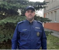 asp. szt. Paweł Kaźmierczak w mundurze. W tle budynek oraz drzewo.