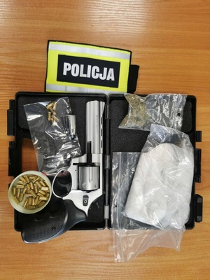 zabezpieczone narkotyki, broń i opaska z napisem policja